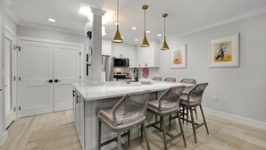 Une cuisine moderne avec des meubles blancs, un îlot central doté de tabourets de bar, un éclairage suspendu et un four à micro-ondes.