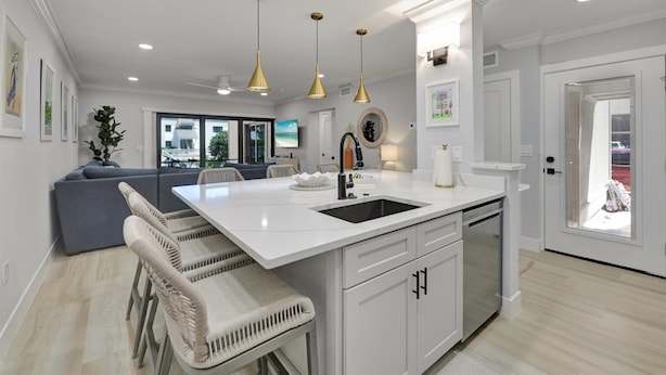 Une cuisine moderne avec des meubles blancs, un îlot central doté d’un évier et des luminaires suspendus.