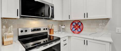 A modern kitchen with white cabinets, a stainless steel stove, and a microwave.
