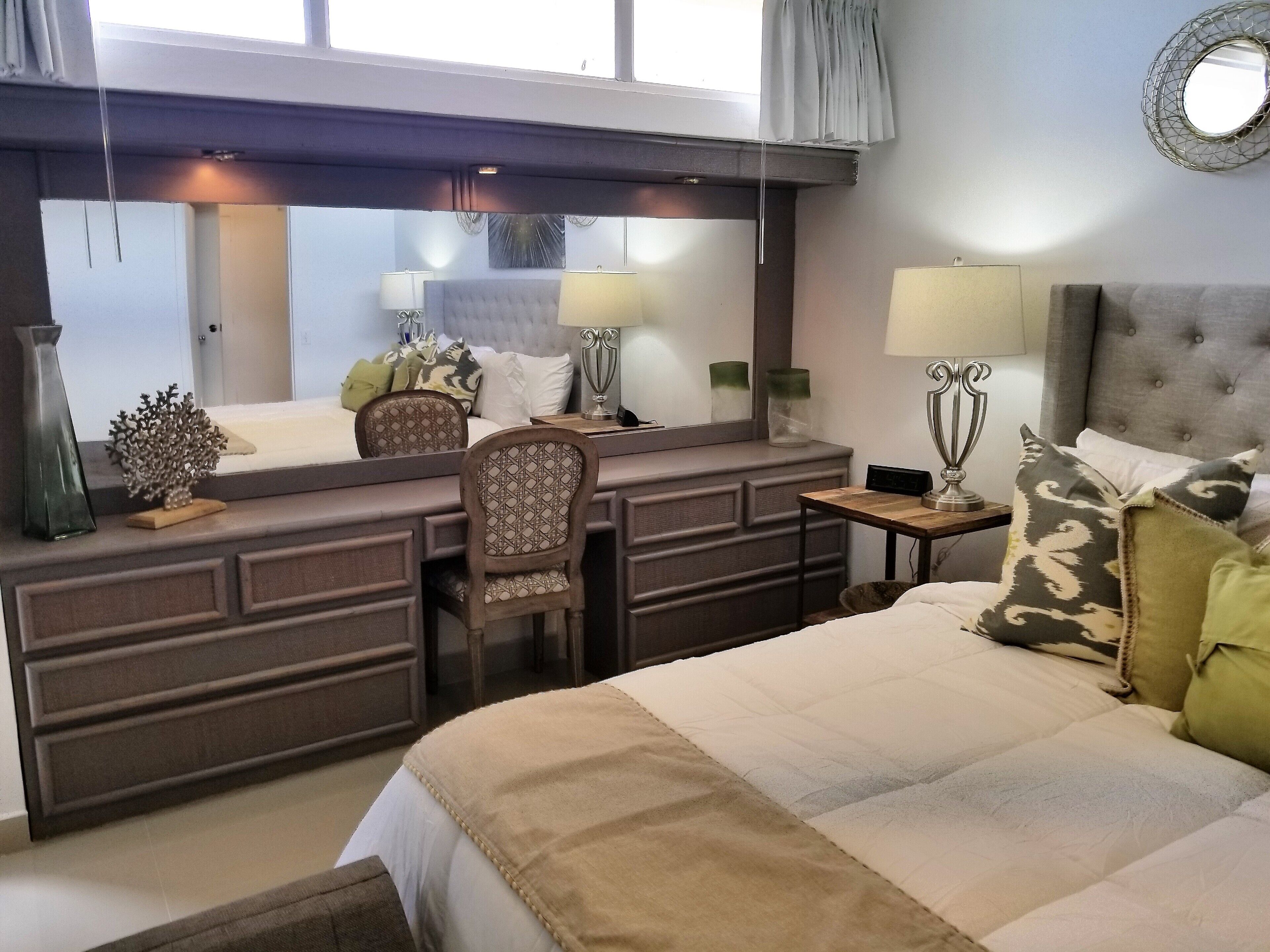 Ein Hotelzimmer mit Bett, Schreibtisch, Stuhl, Spiegel und Lampe.