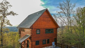 Une cabane en rondins avec des fondations en pierre, une terrasse en bois et une cour clôturée.