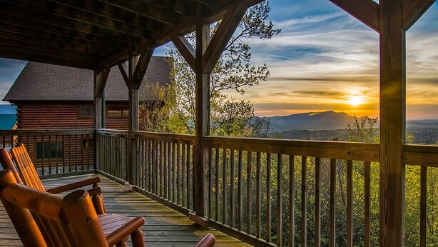 Une terrasse en bois avec deux fauteuils à bascule donnant sur un magnifique coucher de soleil.