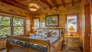 Une chambre dans une cabane en bois, avec un grand lit, une table de chevet, une lampe et un tableau encadré au mur.