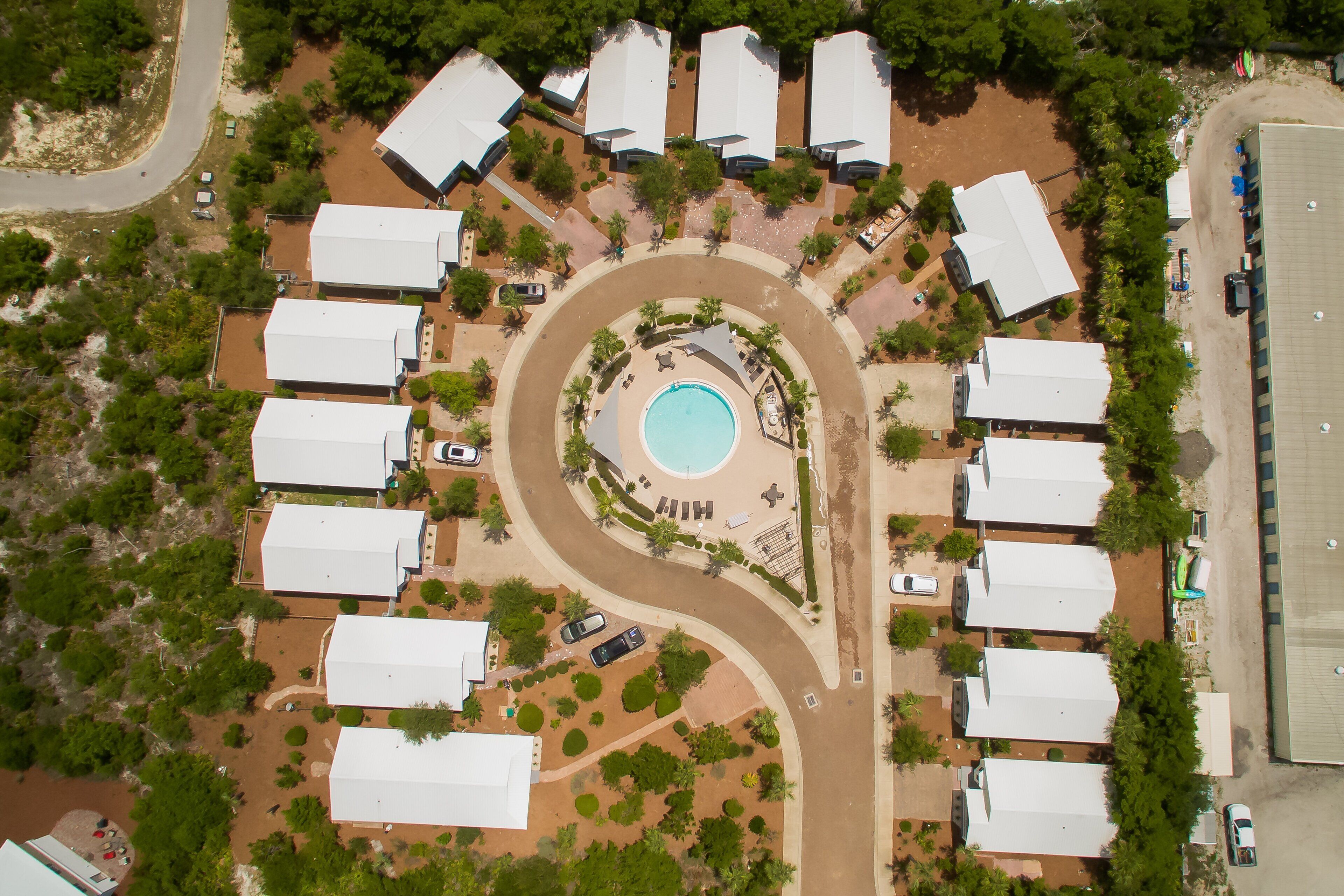 Luchtbeeld van een resort met een centraal gelegen zwembad, gerangschikte villa’s en een kronkelende weg.