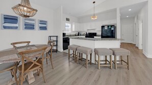 A modern kitchen with white cabinets, a black refrigerator, and a wooden dining table with bar stools. - Pelican House | Walk to Beach + Pool Access in Seagrove (Santa Rosa Beach)