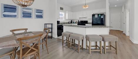 A modern kitchen with white cabinets, a black refrigerator, and a wooden dining table with bar stools.