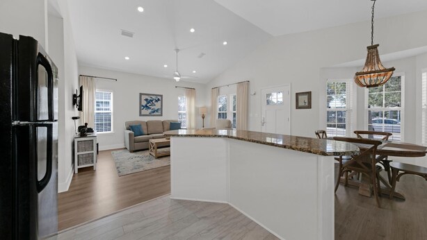 A spacious kitchen with a large island, a dining area with wooden chairs, and a living room with a sofa and a coffee table. - Pelican House | Walk to Beach + Pool Access in Seagrove (Santa Rosa Beach)