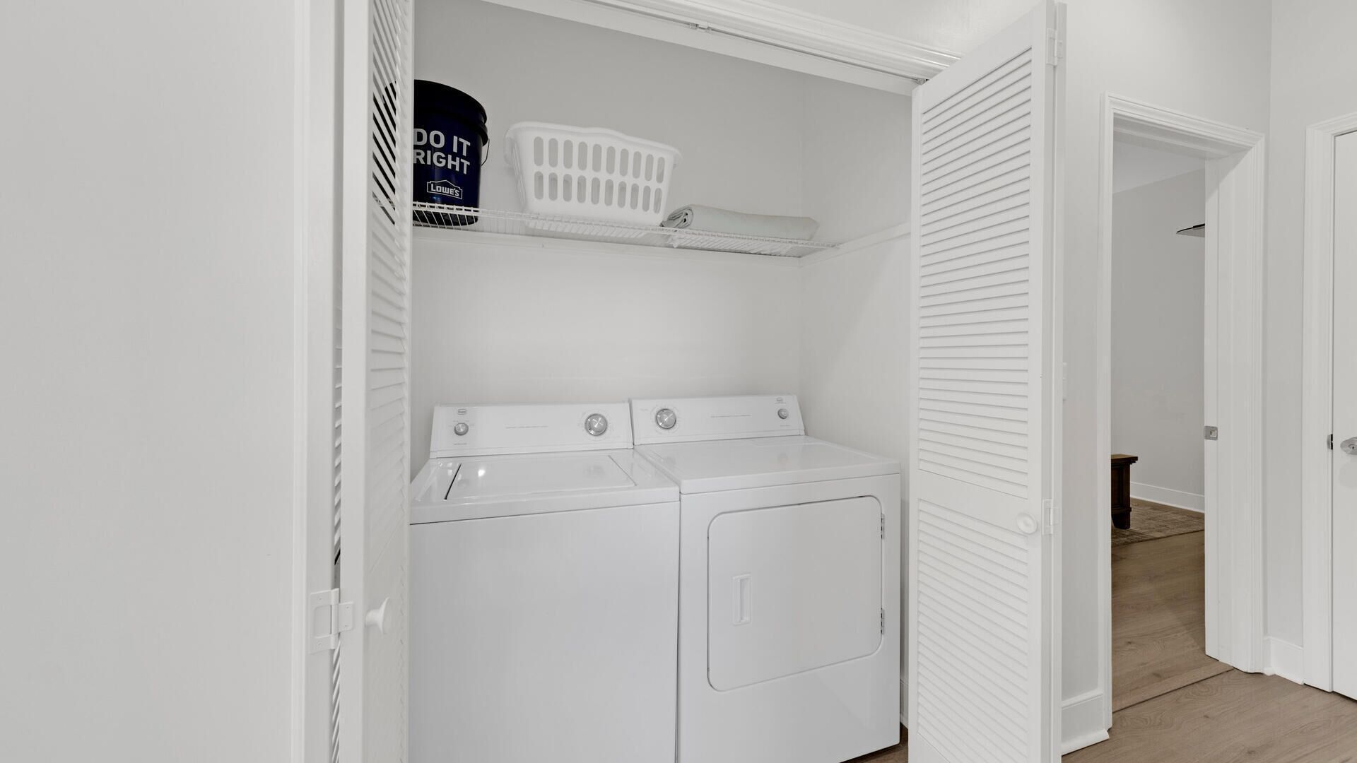 Een wasserette met een voorlader wasmachine en droger, een wasmand en een verfblik van Lowe's op de plank.