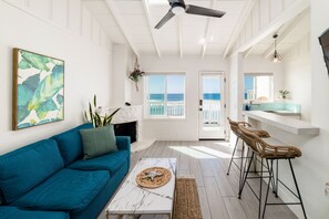 A bright living room with a blue sofa, a white coffee table, and a view of the ocean through large windows. - Pacific Villa #1 | Relaxing Oceanfront Patio Views (Oceanside)