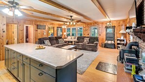 Een gezellig chaletinterieur met houten inrichting, een open haard, een grote bank en een keukenhoek.