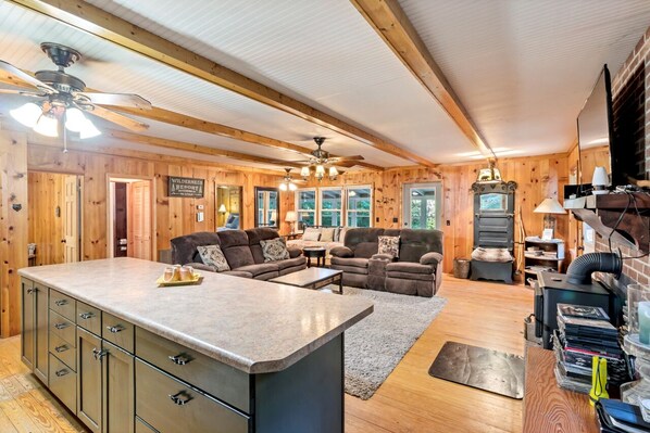A cozy cabin interior with a wooden interior, a fireplace, a large sofa, and a kitchen area.
