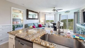 A modern kitchen with granite countertops, a built-in dishwasher, and a large window overlooking a balcony. - Charming & Tranquil Condo at Ocean Pointe-Sleeps 6 (Tavernier)