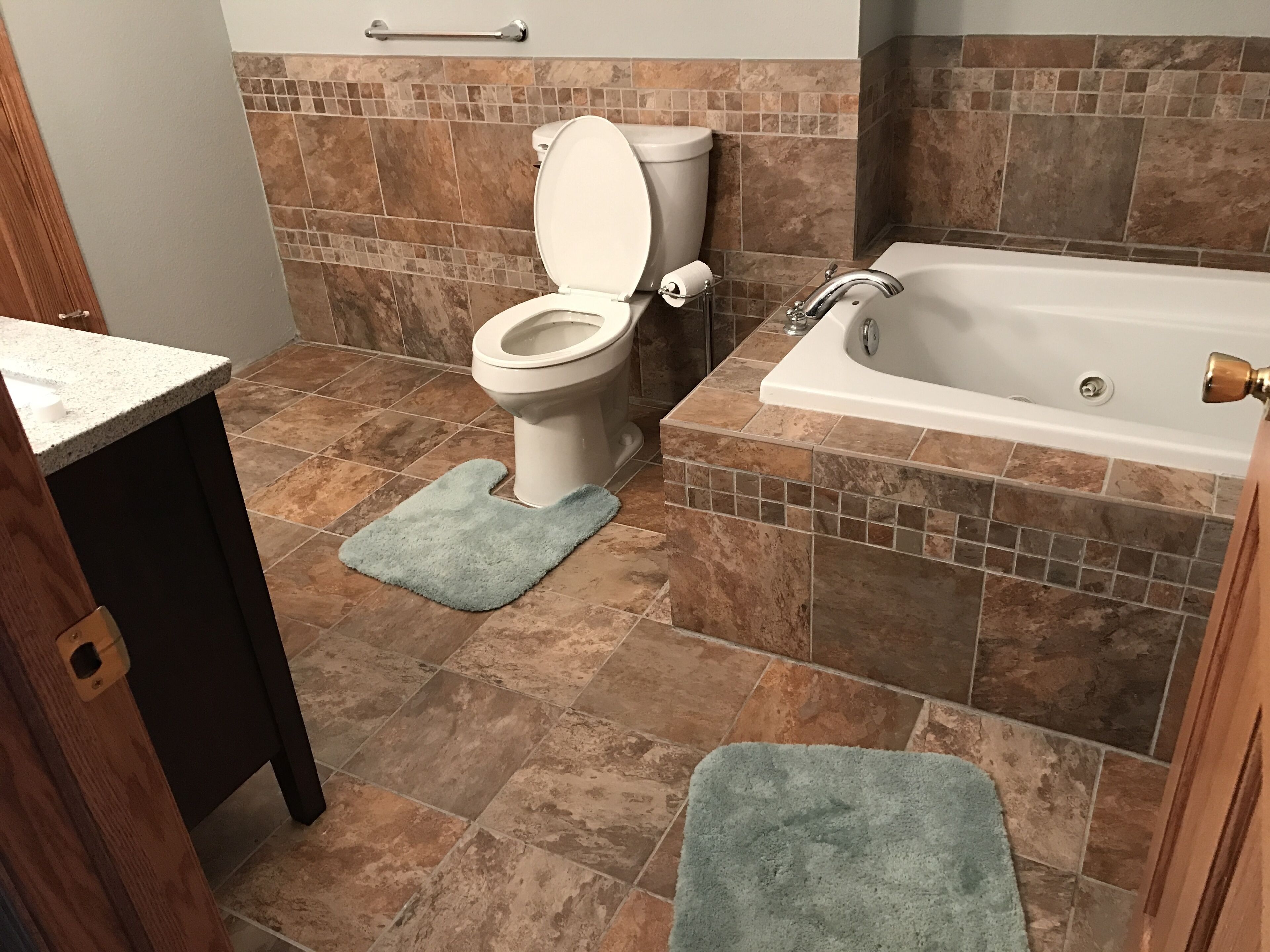 Un baño con inodoro, bañera y dos alfombras de baño azules.