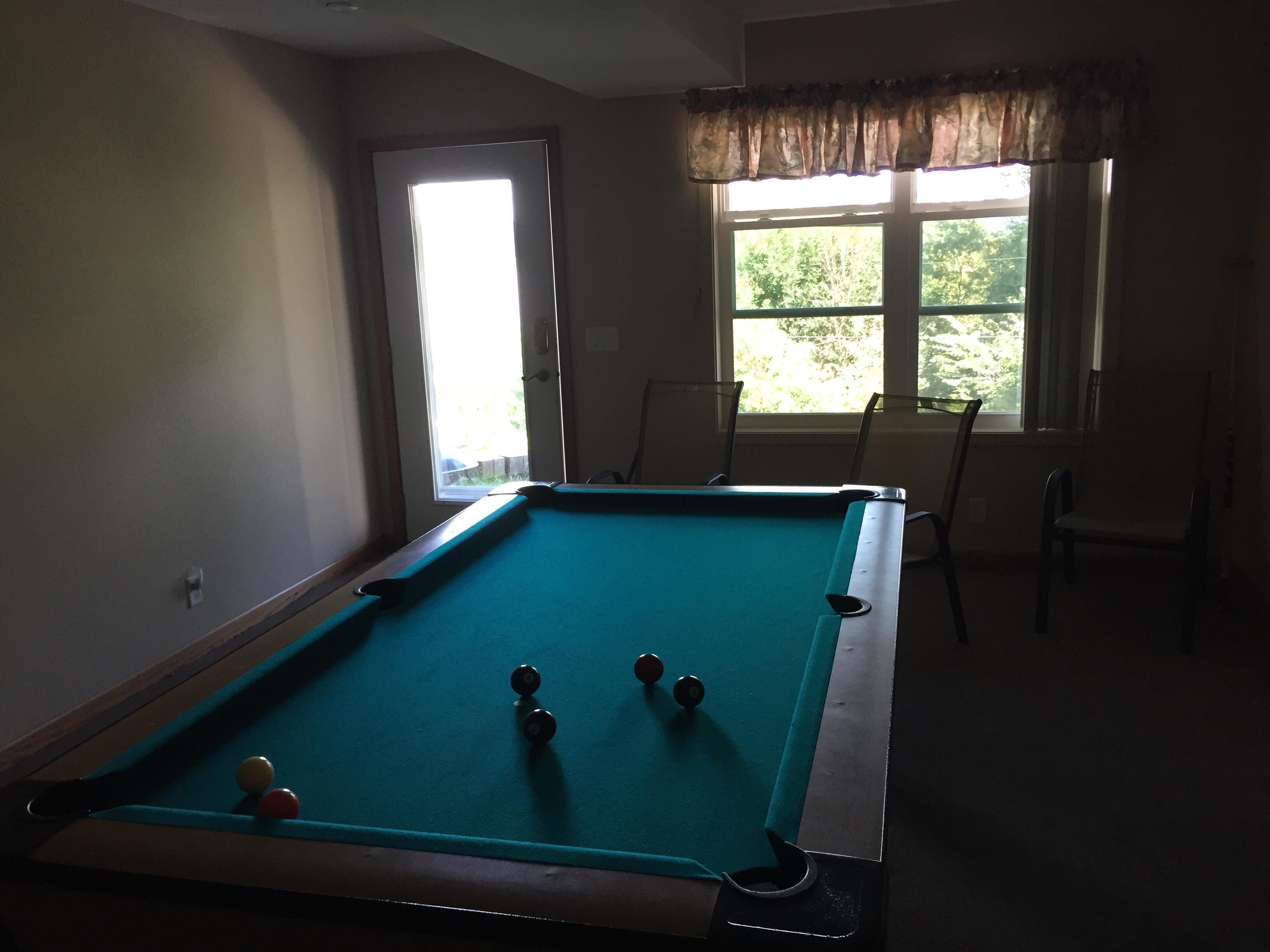 Een pooltafel met ballen in een kamer met een raam en stoelen.