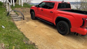Un camioncino rosso parcheggiato su un vialetto sterrato accanto a un edificio con una scala che conduce a un portico.