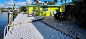 A dock with lounge chairs, a small building with a window, and a paved area.