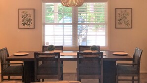A dining area with a dark wooden table, four wicker chairs, a chandelier, and two framed botanical illustrations on the walls. - Bannister Cottage – Lakefront Getaway w/ Dock, Porch & Views, 20 mins to Clemson (Anderson)