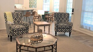 A spacious living room with patterned armchairs, a glass coffee table, and a dining area with wicker chairs. - Bannister Cottage – Lakefront Getaway w/ Dock, Porch & Views, 20 mins to Clemson (Anderson)