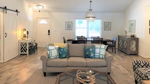 A spacious living room with a sofa, coffee table, and dining area. - Bannister Cottage – Lakefront Getaway w/ Dock, Porch & Views, 20 mins to Clemson (Anderson)