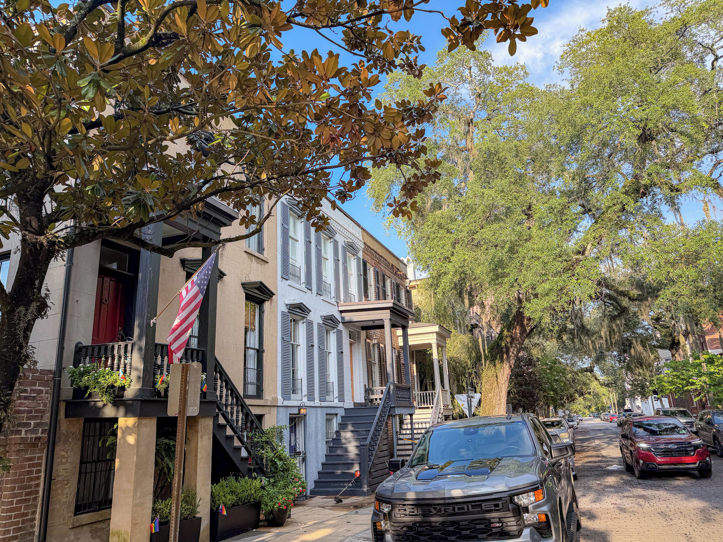A street with parked cars, a building with a flag, and a tree with hanging moss.
