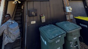 Un bâtiment en briques avec une porte de garage noire portant le numéro « 208 », une petite fenêtre et deux poubelles de recyclage vertes à l’extérieur.