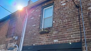 Un bâtiment en briques avec une porte noire portant le numéro « 208 » et une fenêtre agrémentée d’une jardinière.