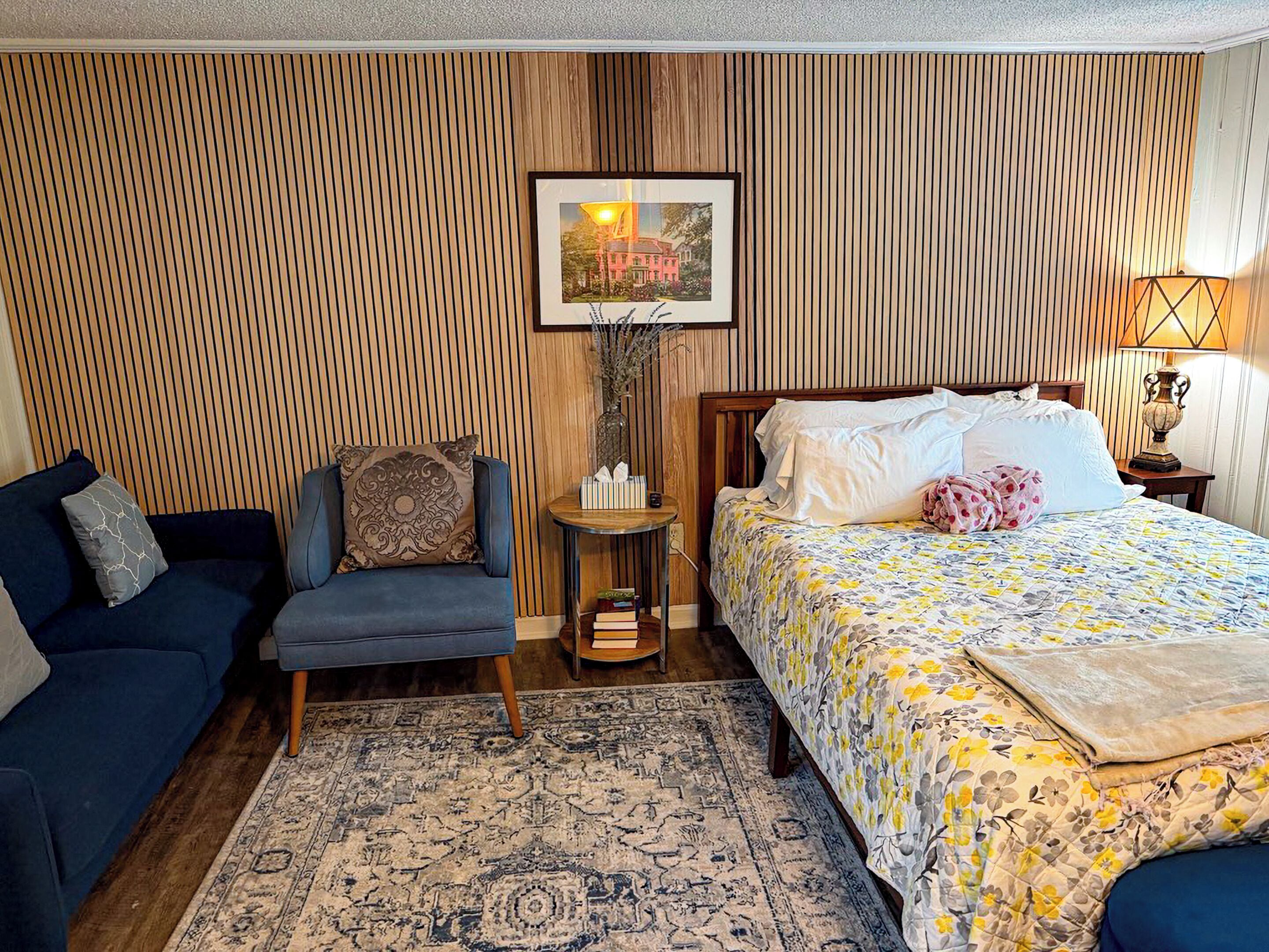 A room with a bed, a sofa, a small table, and a rug.