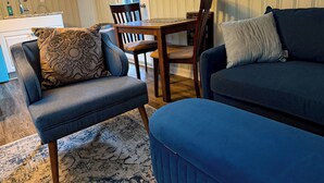 Un salon comprenant un canapé, un fauteuil, une table et une fenêtre avec des stores.