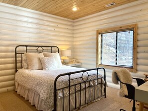 A cozy bedroom with a metal bed frame, a wooden ceiling, and a window with blinds.