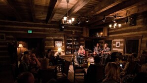 A rustic wooden interior with a band performing on stage, surrounded by seated patrons.