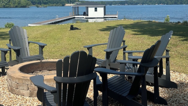 Een terras aan het meer met Adirondack-stoelen, een vuurkuil en een klein vakantiehuis.