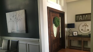 Een moderne woonkamer met een donkere muur, een houten deur met een krans, een blauw vloerkleed, en een eetgedeelte met een tafel en stoelen.