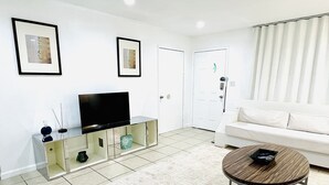 A modern living room with a flat-screen TV on a glass cabinet, a white sofa, and a round wooden coffee table. - 2BRpartment,LasVegas,Strip,Pet-friendly,Lvcc,SALE,BestSpot,Sema Show,Labor day (Las Vegas)