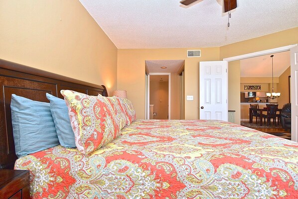 A hotel room with a large bed, a wooden headboard, and a ceiling fan.