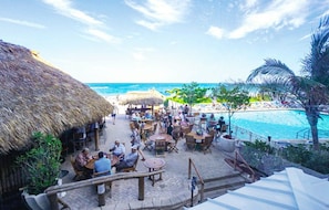 Relax in a shaded outdoor space with ocean views, featuring thatched-roof structures, tables, and chairs.