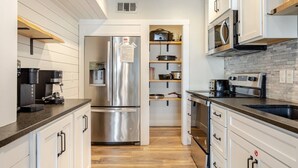 Una cocina moderna con electrodomésticos de acero inoxidable, estantes de madera y armarios blancos.