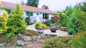 A house with a red roof, surrounded by a garden with various plants and a fire pit. - Reconnect ~ Relax ~  Rejuvenate ~ Explore ~  Larch Avenue Getaway (Port Angeles)