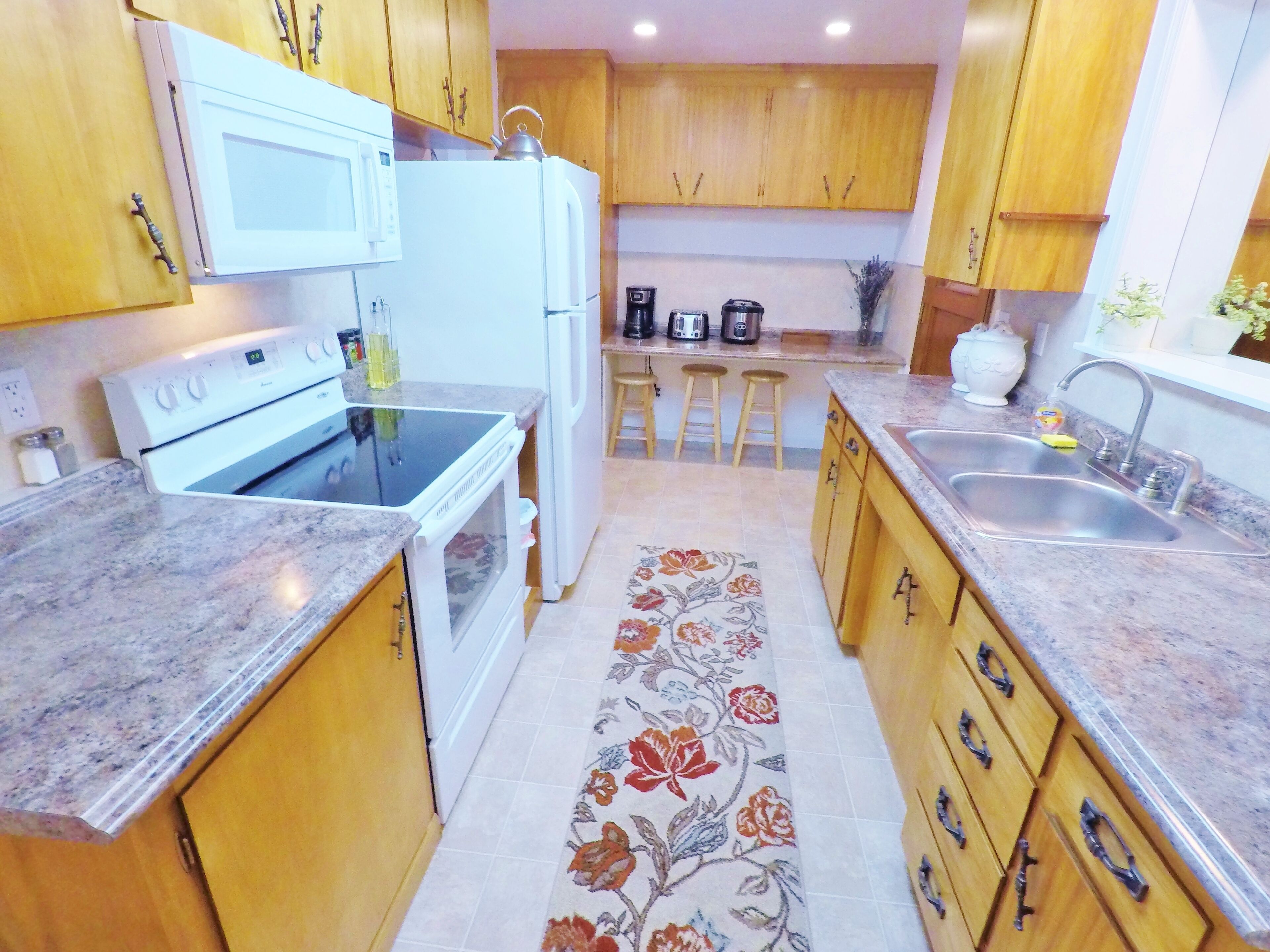 A kitchen with wooden cabinets, a microwave, a stove, a refrigerator, a sink, and a coffee maker.