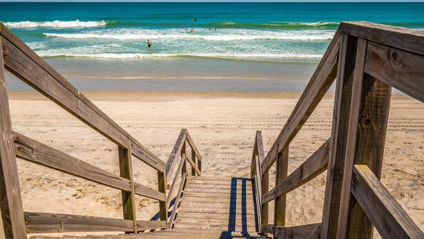 A wooden boardwalk leading to a sandy beach with the ocean in the background.