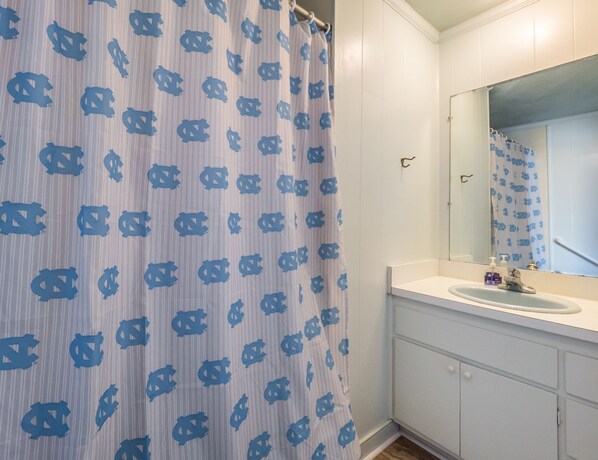 Une salle de bain avec un rideau de douche à rayures, un lavabo, un miroir et un meuble.