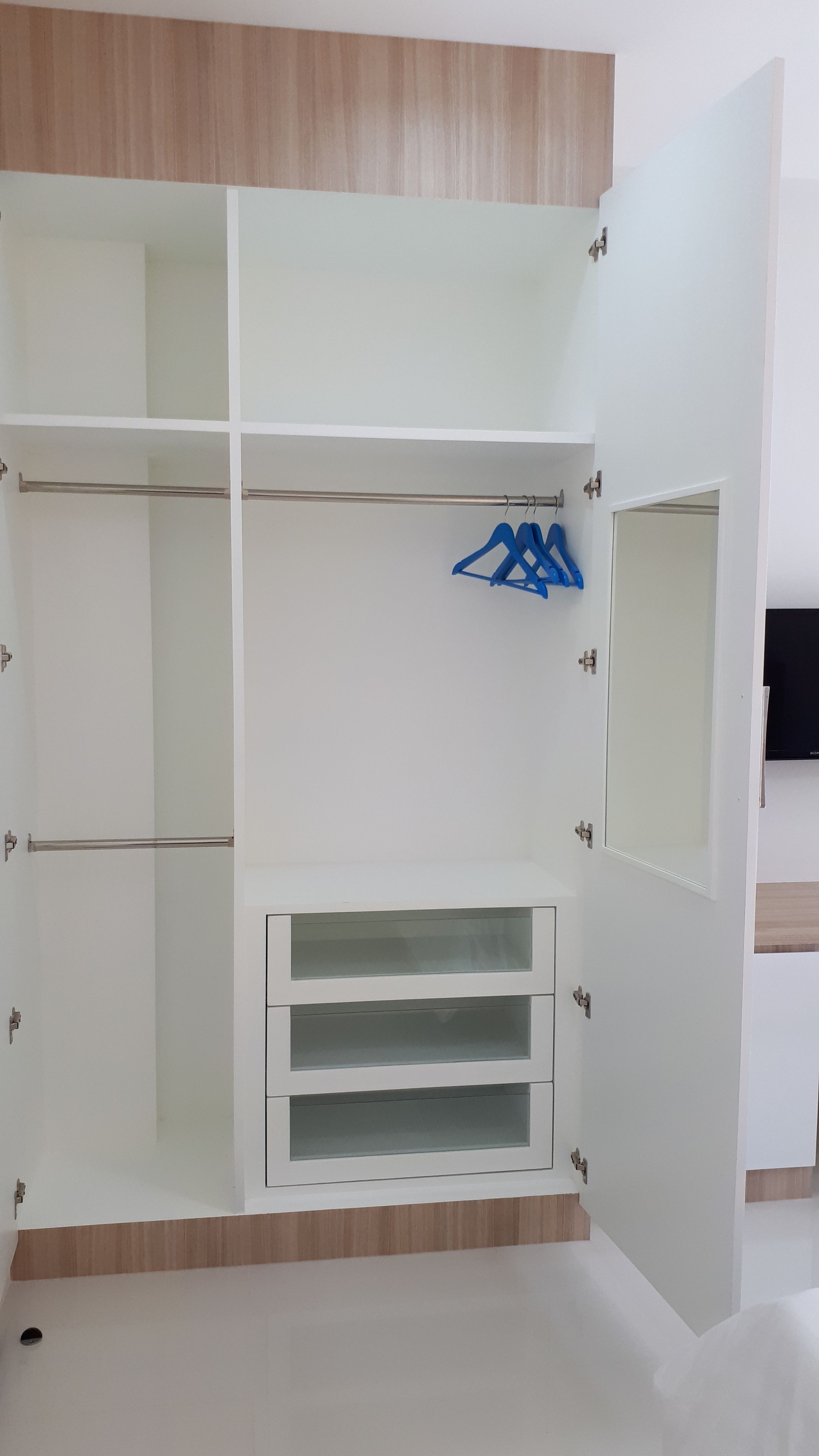 A walk-in closet with open doors, featuring a mirrored section, a hanging rod, and a built-in storage unit.