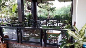 An outdoor cafe with tables and chairs, surrounded by greenery and a view of the city.
