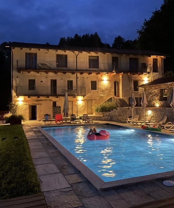 A two-story building with a swimming pool, lounge chairs, and a red inflatable float.