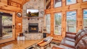 Interior acogedor de una cabaña con chimenea de piedra, paredes de madera, sofá de cuero y televisor sobre la chimenea.