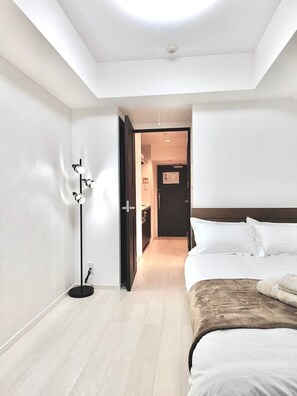 A modern hotel room with a large bed, a standing floor lamp, and a door leading to a hallway.