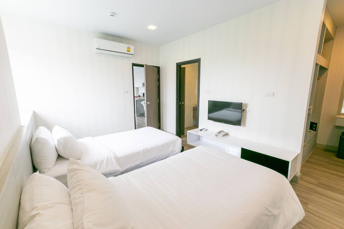 A hotel room with two beds, a TV, a small desk, and a door leading to a bathroom.