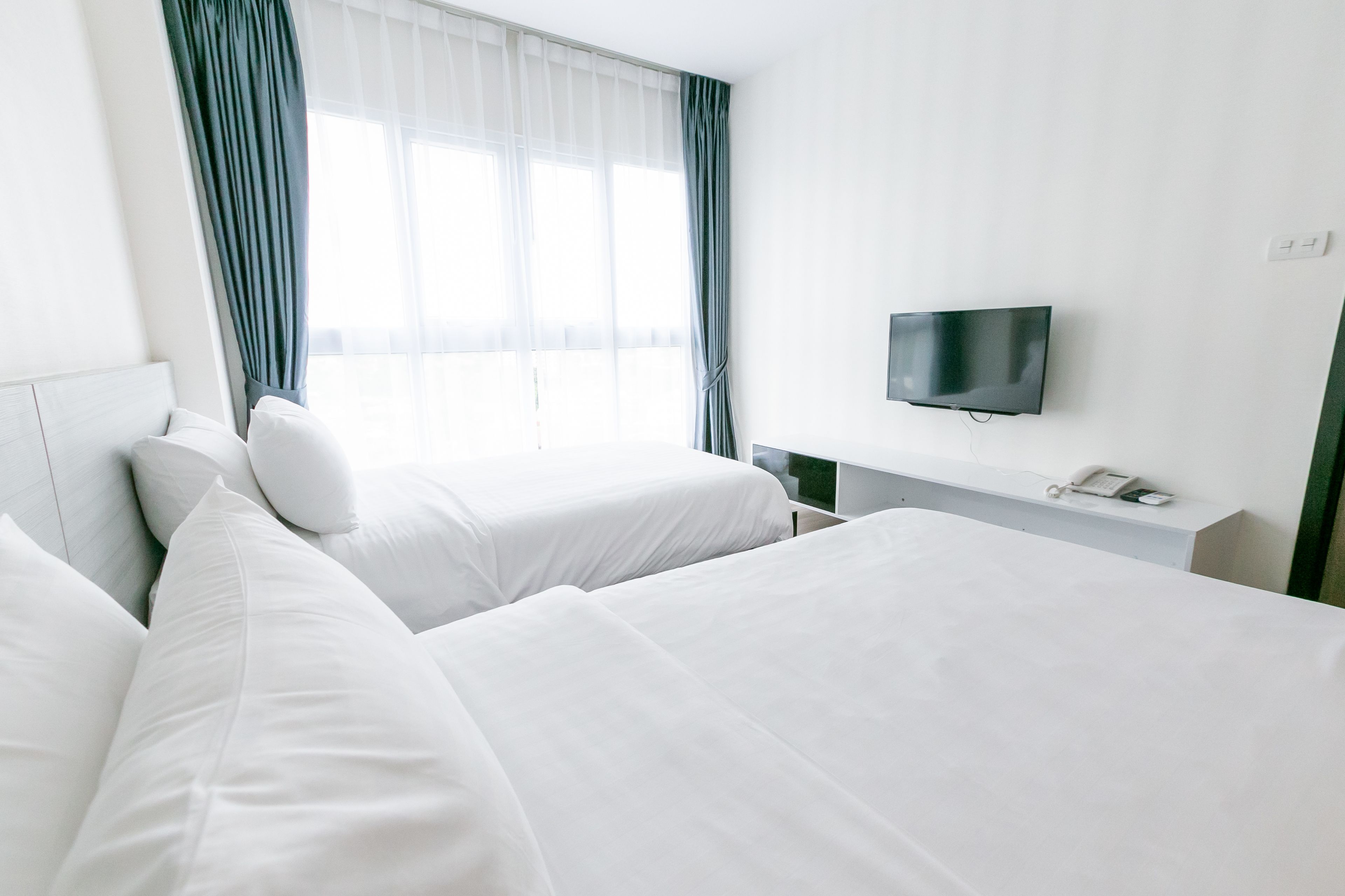 A hotel room with two beds, a TV mounted on the wall, and a window with curtains.