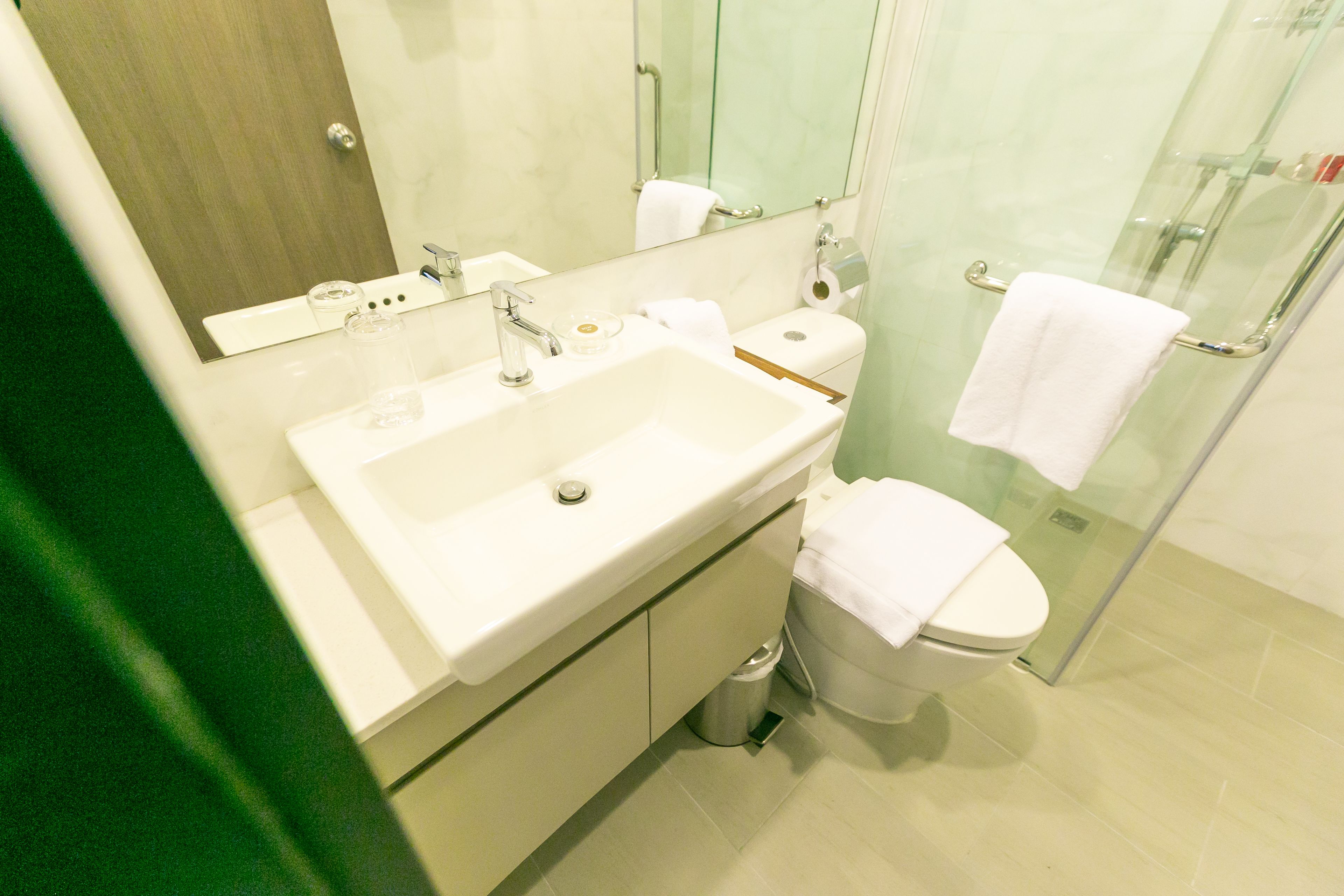 A modern bathroom with a sink, mirror, toilet, and glass shower enclosure.