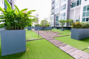 A courtyard with artificial grass, a wooden pathway, and large planters with green plants.