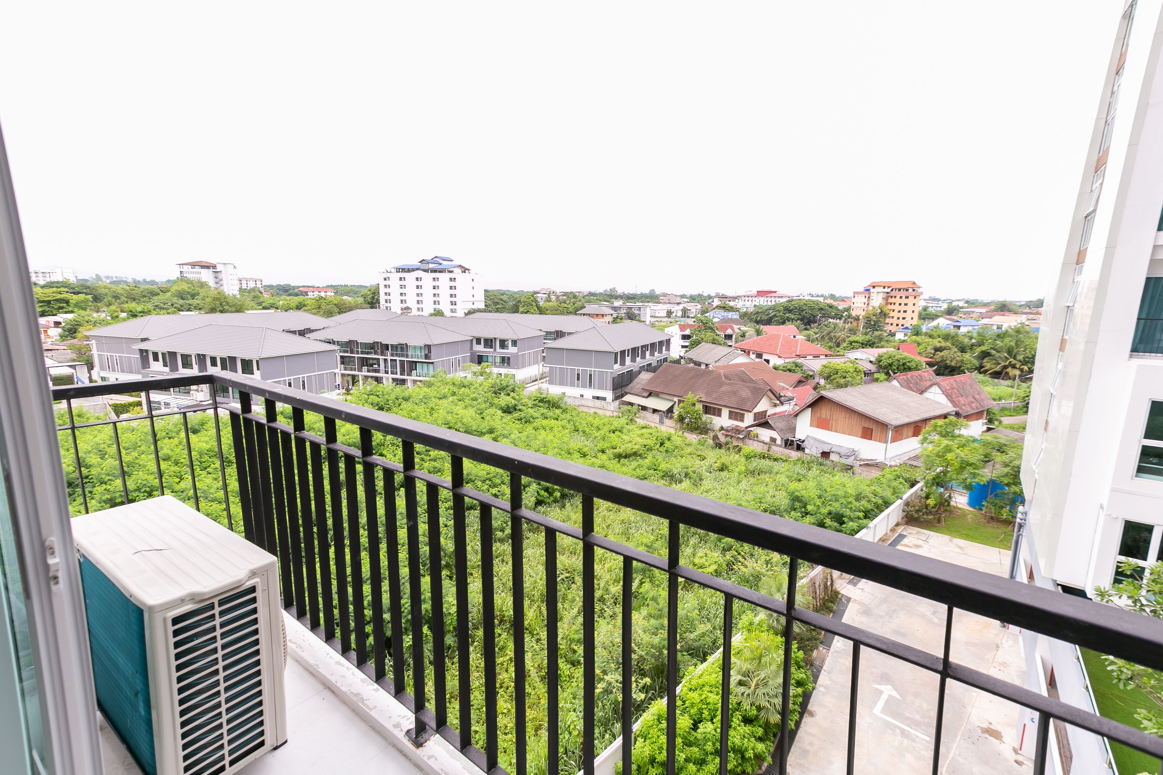 A residential area with modern buildings, a balcony with a black railing, and an air conditioning unit.